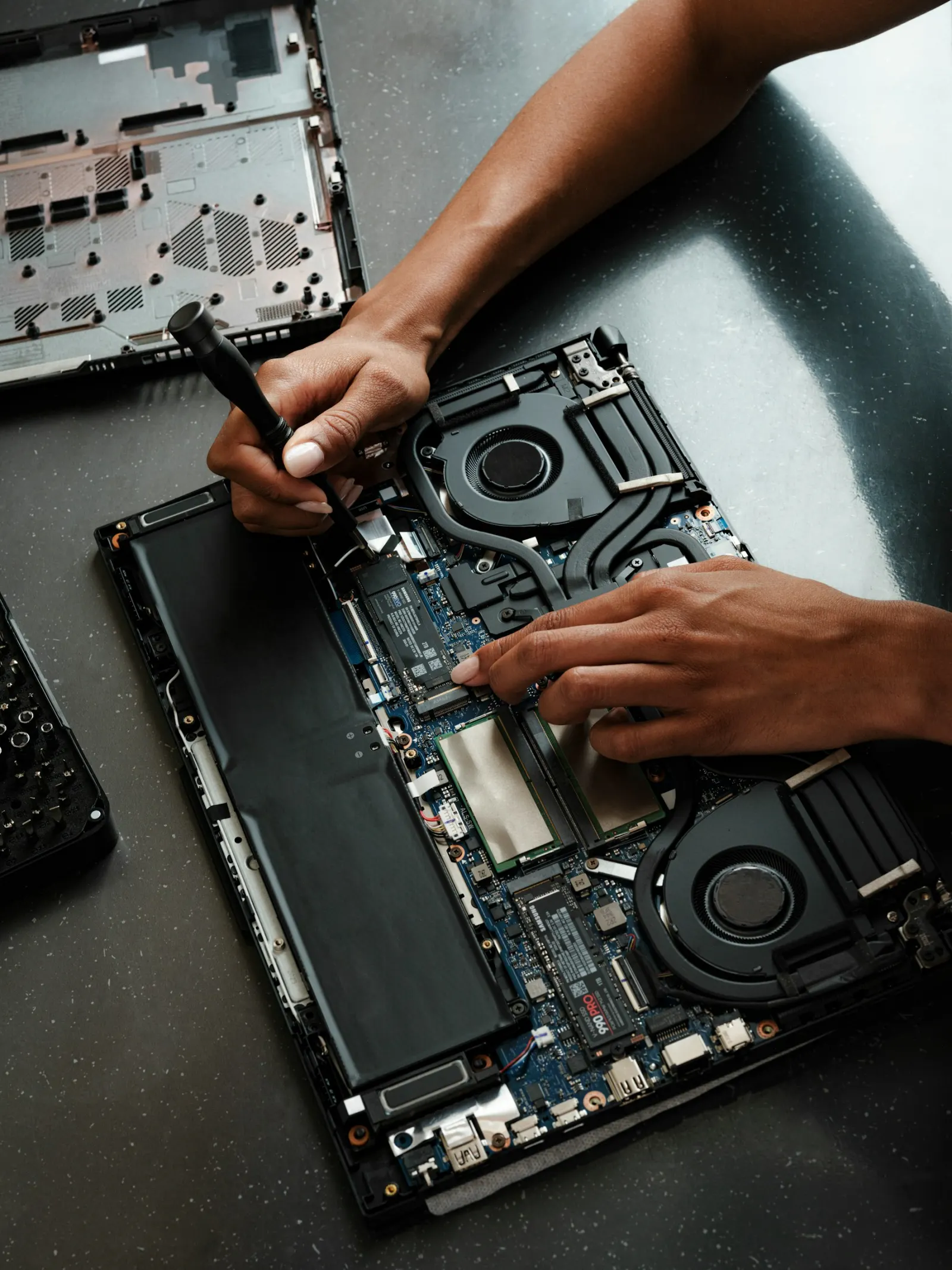 Mains d'un technicien intervenant à l'intérieur d'un ordinateur portable ouvert